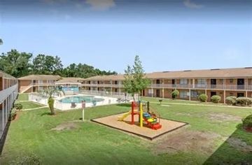 Jacksonville apartment for rent - A playground with a slide and a tree in the middle of a grassy area in front of a building.