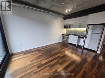 Toronto (Moss Park) condo for rent - A room with wooden flooring and a kitchen area in the background.