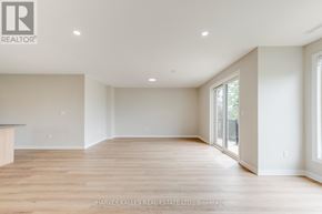 Toronto (Downsview-Roding-Cfb) multi-family for rent - A spacious room with wooden flooring and white walls, with a logo of a realtor in the top left corner.