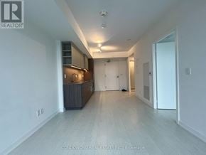 Toronto (Waterfront Communities) condo for rent - A spacious, empty room with a kitchen area in the background.