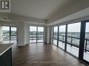 Clarington (Bowmanville) condo for rent - A spacious room with wooden floors and large windows overlooking a cityscape.
