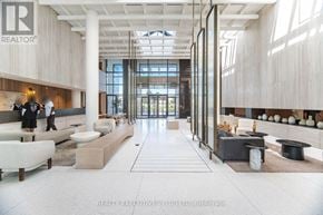 Vaughan (Vaughan Corporate Centre) condo for rent - A modern lobby with a reception desk and a person standing by the window.