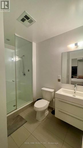 Toronto (Kensington-Chinatown) condo for rent - A white toilet sits in a bathroom next to a sink and a glass shower stall.