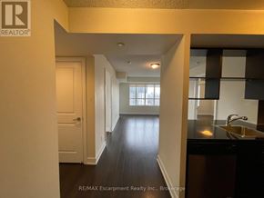Toronto (Etobicoke West Mall) condo for rent - A hallway with a white door and a kitchen area with a sink and cabinets.