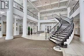 Toronto (Newtonbrook West) condo for rent - A grand staircase with a metal railing and a chandelier hangs in a large, open space with white columns and a marble floor.