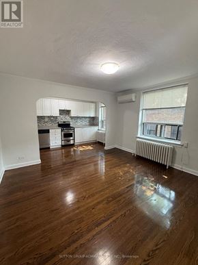 Toronto (Yonge-Eglinton) multi-family for rent - A room with wooden floors and a kitchen area in the background.