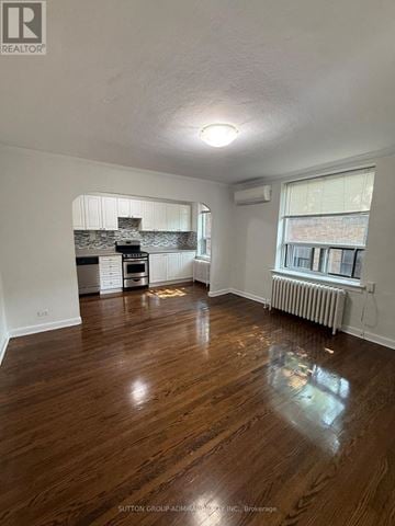 Toronto (Yonge-Eglinton) multi-family for rent - A room with wooden floors and a kitchen area in the background.