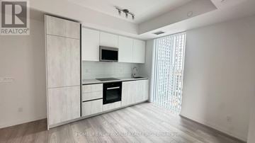 Toronto (Waterfront Communities) condo for rent - A modern kitchen with white cabinets and a black oven.