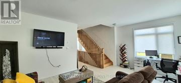 Pickering (Village East) townhouse for rent - A living room with a television and a staircase in the background.
