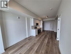 Brantford condo for rent - A spacious room with wooden flooring and a kitchenette in the corner.