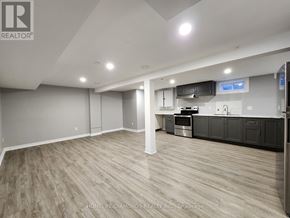 Thorold (Confederation Heights) apartment for rent - A spacious room with wooden flooring and a kitchen area with black cabinets.