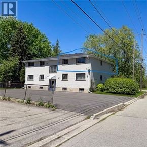 Brantford apartment for rent - A two-story house with a white and blue exterior is surrounded by a fence and trees.