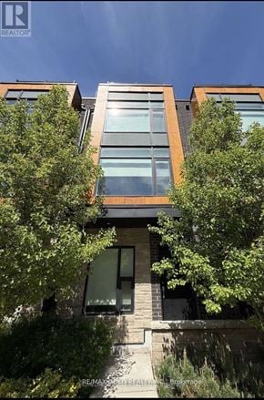 Brampton (Fletcher's Creek South) townhouse for rent - A modern house with a glass window is surrounded by green trees.
