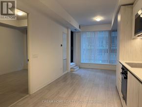 Toronto (Waterfront Communities) condo for rent - A spacious room with wooden flooring and a kitchen area with white cabinets.