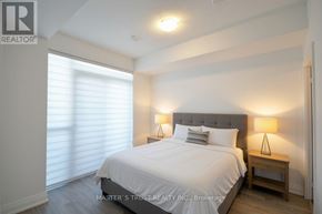 Oakville (Co Central) condo for rent - A bedroom with a large bed, a nightstand, and a window with blinds.