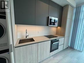 Toronto (Waterfront Communities) condo for rent - A modern kitchen with a washing machine on the left and a microwave above the stove.
