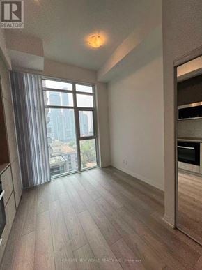 Toronto (Waterfront Communities) condo for rent - A spacious room with wooden flooring and a large window overlooking a cityscape.