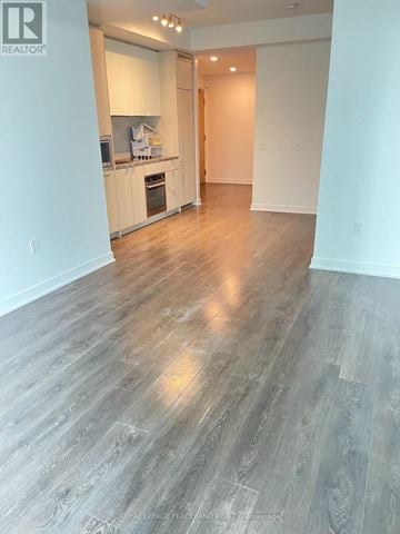 Toronto (Waterfront Communities) condo for rent - A spacious room with wooden flooring and a kitchen area in the background.