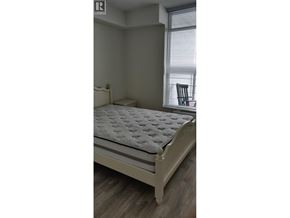 Burnaby apartment for rent - A white bed with a grey patterned mattress pad in a room with a window.