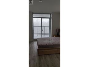 Burnaby apartment for rent - A bedroom with a bed, wooden floor, and a glass door leading to a balcony.