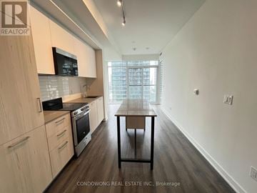 Toronto (Church-Yonge Corridor) condo for rent - A kitchen with wooden cabinets and a black microwave above the stove.