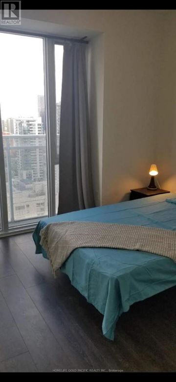 Toronto (Church-Yonge Corridor) condo for rent - A bedroom with a bed covered in a blue sheet and a window with curtains.
