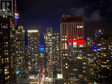 Toronto (Waterfront Communities) condo for rent - A cityscape at night with tall buildings and a bridge in the distance.