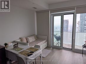 Mississauga (City Centre) condo for rent - A bedroom with a bed, desk, and chair in front of a window with a view of a cityscape.