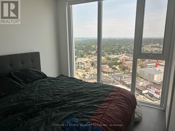 Barrie (City Centre) condo for rent - A bedroom with a large window overlooking a cityscape.