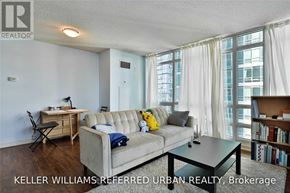 Toronto (Waterfront Communities) condo for rent - A living room with a grey couch, a black coffee table, and a window with white curtains.