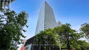 Toronto (Church-Yonge Corridor) condo for rent - A tall building with a glass facade is surrounded by trees and has a sign that reads "Prompton Real Estate Services Corp. Brokerage".