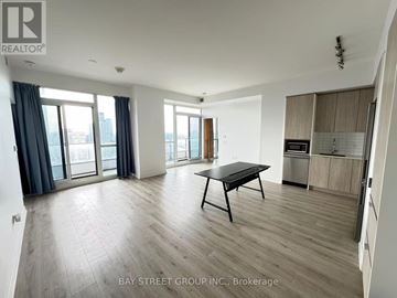 Toronto (North St. James Town) condo for rent - A spacious living room with a dining table and a view of the city through the windows.