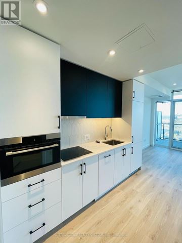 Kitchener condo for rent - A modern kitchen with white cabinets and a black backsplash.