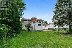 Windsor apartment for rent - A white house with a brown roof is surrounded by green grass and trees.