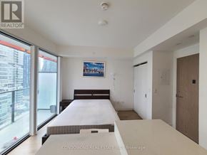 Toronto (Waterfront Communities) condo for rent - A bedroom with a large bed and a balcony overlooking a cityscape.