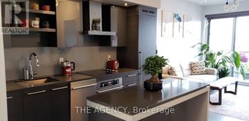 Toronto (Niagara) condo for rent - A modern kitchen with a large island and a living area with a couch and plants.