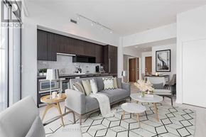 Toronto (Bayview Village) condo for rent - A modern living room with a grey sofa, a coffee table, and a kitchen area in the background.