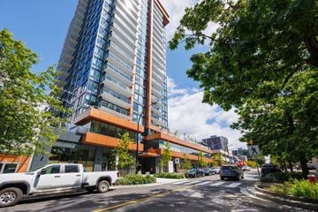 North Vancouver apartment for rent - A modern building with a glass facade is surrounded by trees and vehicles on the street.