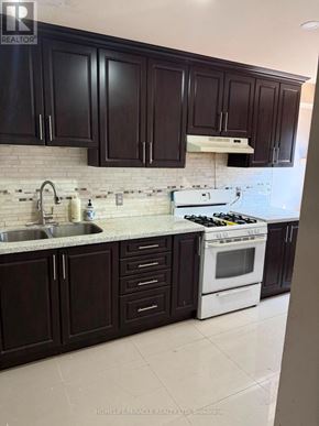 Toronto (Mount Olive-Silverstone-Jamestown) townhouse for rent - A kitchen with dark brown cabinets and a white stove top oven.