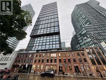 Toronto condo for rent - A tall building with a glass facade stands next to a shorter building with a brick facade.