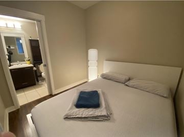 Surrey apartment for rent - A bed with a white comforter and a blue pillow case is in a room with a mirror and a lamp.