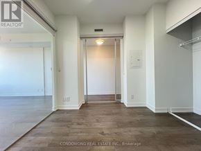 Toronto (South Parkdale) condo for rent - A spacious room with wood flooring and white walls.