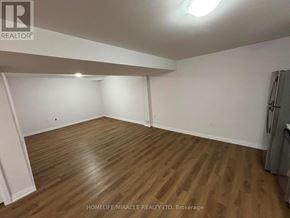 Bradford West Gwillimbury (Bradford) apartment for rent - A room with wooden flooring and white walls, with a refrigerator on the right side.