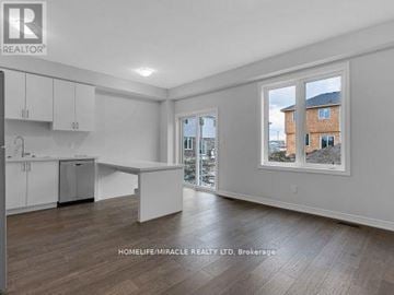 Hamilton (Hill Park) townhouse for rent - A spacious room with wooden floors and white walls, featuring a kitchen area with cabinets and a window showing an outdoor view.