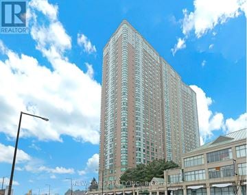 Toronto (Woburn) condo for rent - A tall building with a glass facade stands in front of a blue sky with clouds.