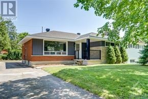 Ottawa apartment for rent - A house with a brick facade and a black door is surrounded by greenery.