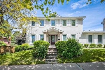 Toronto apartment for rent - A white house with a brown door and windows is surrounded by greenery.