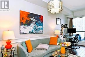 Toronto (Willowdale East) condo for rent - A living room with a grey couch, a painting on the wall, and a glass table with a vase of flowers on it.