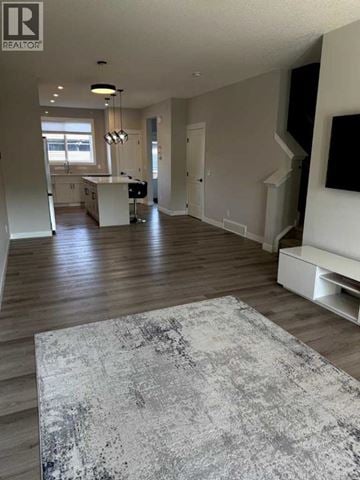 Calgary apartment for rent - A large, open living room with a grey rug in the foreground and a kitchen area in the background.