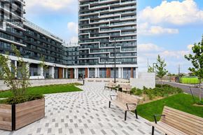 Markham (Greensborough) condo for rent - A modern building with a glass facade and a courtyard with benches and trees.